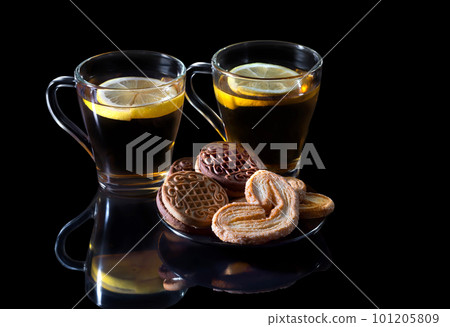 Black tea with a lemon, with cookies in a glass cup, with reflection on a black background 101205809