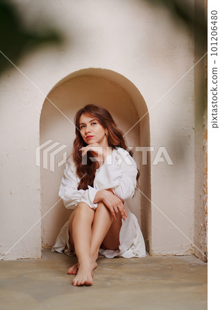 a woman in a white dress barefoot sitting on the floor in an arch on the wall a woman in a white dress barefoot sitting on the floor in an arch on the wall 101206480