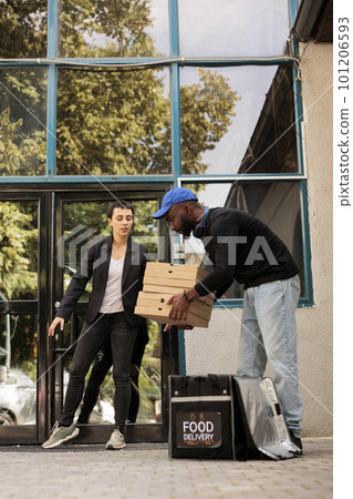 Customer receiving pizza boxes pile, courier taking out order from thermal backpack outdoors. Food delivery service, pizzeria african american deliveryman holding takeaway lunch 101206593