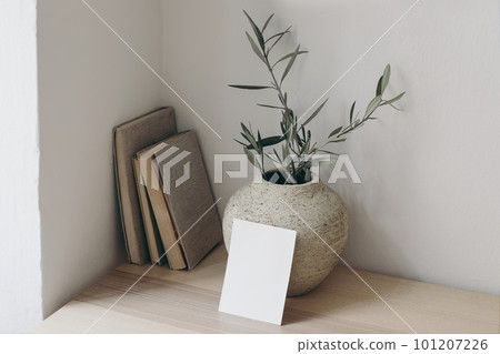 Summer wedding stationery. Closeup of blank greeting card, invitation. Textured vase with olive branches and old books on wooden table. Mediterranean design. Elegant working space, home office. 101207226