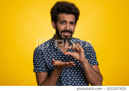 Indian man showing a little bit gesture with sceptic smile showing minimum sign measuring small size 101207420