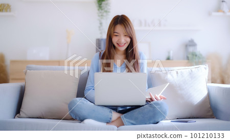 Young asian woman using laptop while seated on couch at home 101210133