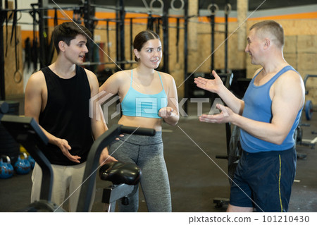 Sporty young girl chatting with male friends in gym Sporty young girl chatting with male friends in gym 101210430