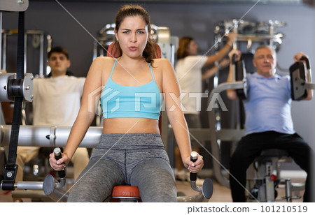 Portrait of young woman during workout with power exercise machine in gym 101210519