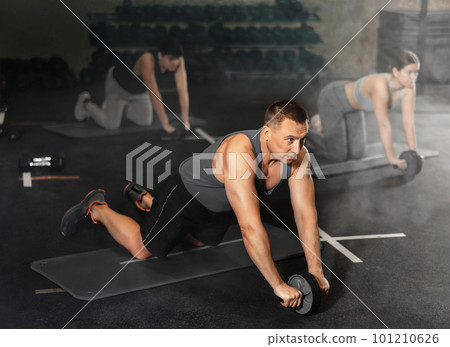 Man doing wheel rollout exercise at workout routine in gym Man doing wheel rollout exercise at workout routine in gym 101210626