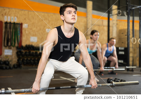 Motivated CrossFit male athlete lifting heavy body bar or barbell during group training in gym. Functional training concept 101210651