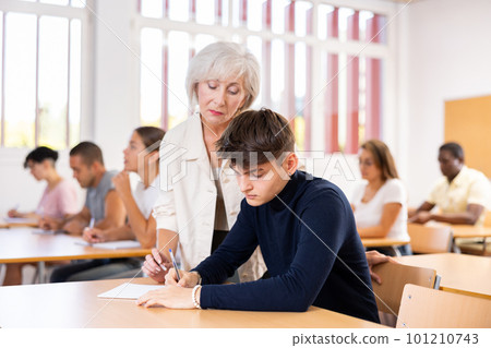 Aged female teacher helping guy student solving problem at lesson Aged female teacher helping guy student solving problem at lesson 101210743