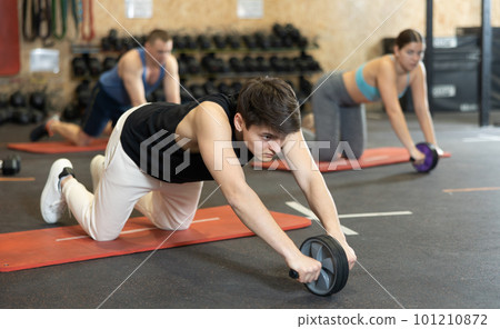 Motivated young man practicing exercises with abs roller in gym Motivated young man practicing exercises with abs roller in gym 101210872
