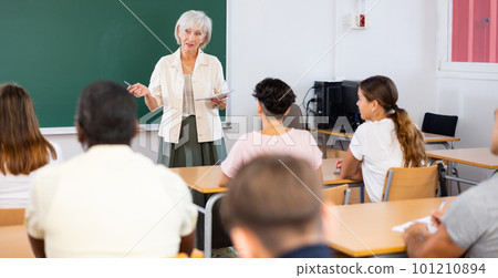 Woman teacher explaining new theme to students during class in university indoors Woman teacher explaining new theme to students during class in university indoors 101210894