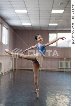 Graceful Asian ballerina in a blue bodysuit and a beige skirt is rehearsing in a dance class.  101211295