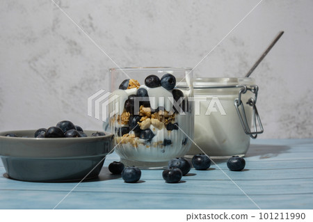 Preparing step by step Morning granola breakfast with homemade greek yogurt, blueberries in glasses on blue wooden background. Healthy diet Crunchy granola with yogurt nuts and blueberries 101211990