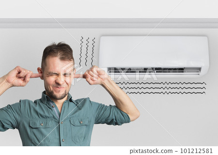 The air conditioner is broken - makes loud noises, noises and vibrations. Man covering his ears 101212581