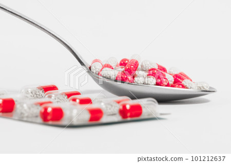 Blister and spoon with red pills on a white background. Drug overuse and antibiotic resistance 101212637