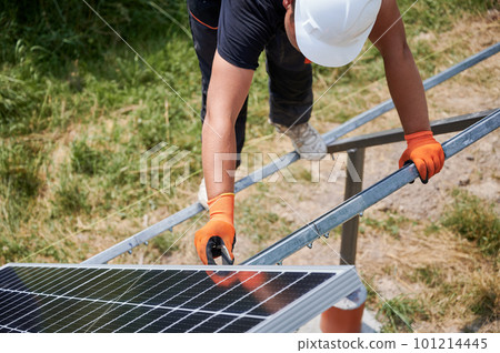 Male worker mounting photovoltaic solar panel system outdoors. Man engineer placing solar module on metal rails, wearing construction helmets and work gloves. Renewable and ecological energy. Male worker mounting photovoltaic solar panel system outdoors. Man engineer placing solar module on metal rails, wearing construction helmets and work gloves. Renewable and ecological energy. 101214445
