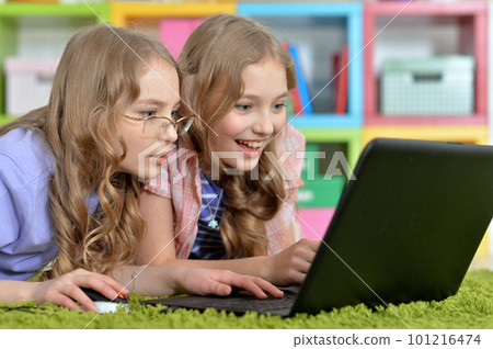 Two pretty little girls lying on floor and using laptop Two pretty little girls lying on floor and using laptop 101216474
