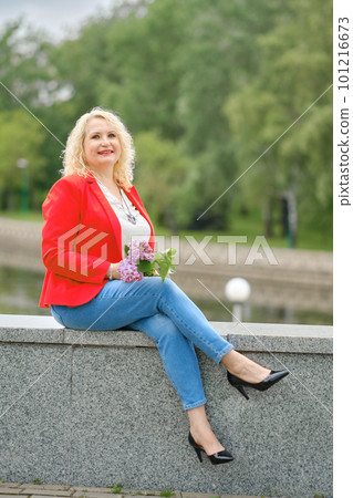 Happy middle-aged woman sits on the embankment in a city park Happy middle-aged woman sits on the embankment in a city park 101216673