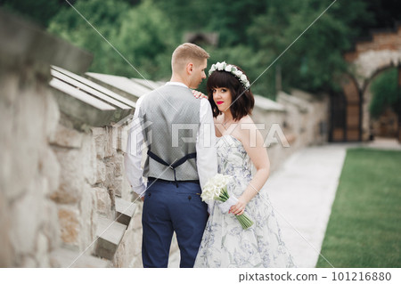Romantic, fairytale, happy newlywed couple hugging and kissing in a park, trees in background 101216880