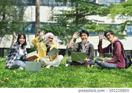 Group of young students sitting outside of university building and waving hands to camera. Youth lifestyle and education concept 101218803