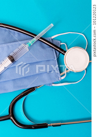 Two blue cotton medical masks, stethoscope and syringe on blue background Two blue cotton medical masks, stethoscope and syringe on blue background 101220123