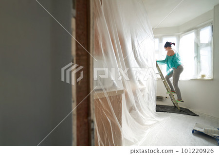 Woman stands on the stairs and paints the wall with a roller Woman stands on the stairs and paints the wall with a roller 101220926