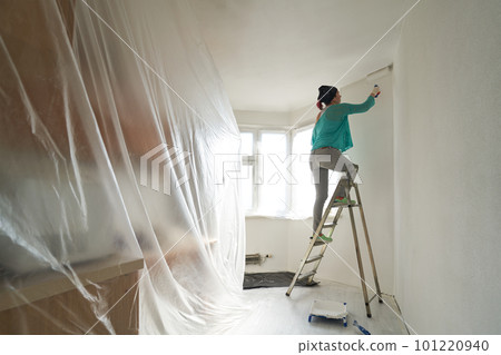 Woman stands on the stairs and paints the wall with a roller Woman stands on the stairs and paints the wall with a roller 101220940