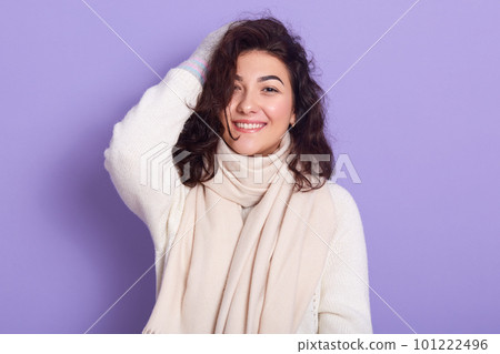 Closeup portrait of smiling adorable female having black curly hair, looking directly at camera, wearing warm items of clothes, smiling sincerely, being fond of white clothes. Winter concept. 101222496