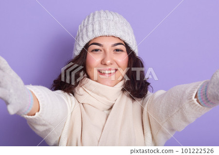 Portrait of good looking young lady extending her hands, smiling sincerely, looking directly at camera, wearing white hat, scarf, gloves and sweater, being in high spirits. People and winter concept. Portrait of good looking young lady extending her hands, smiling sincerely, looking directly at camera, wearing white hat, scarf, gloves and sweater, being in high spirits. People and winter concept. 101222526