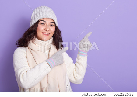 Adorable cheerful model standing isolated over lilac background, raising her hands up, making gesture, smiling, having black hair, showing direction, wearing warm clothes. Copyspace for advertisement. 101222532