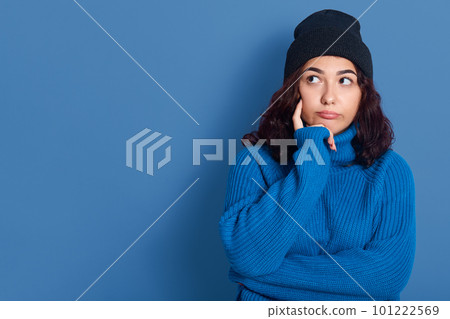 Horizontal indoor picture of thoughtful adorable beautiful young woman looking aside, touching cheeck with finger, being upset, having pensive facial expression. Copyspace for advertisement. 101222569