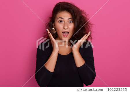 Close up portrait of young beautiful girl with long wavy hair looks excited, keeps her mouth opened and hands raised, isolated over pink wall. Shocked, surprised, stunned woman. Human emotions concept 101223255