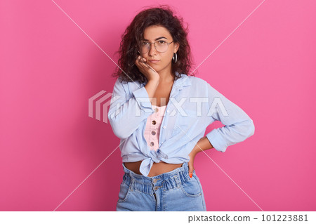 Attractive woman in eyeglasses and fashionable outfit with thoughtful facial expression, thinks about question, raises eyebrows, keeps hand under chin, isolated on pink background. People concept. Attractive woman in eyeglasses and fashionable outfit with thoughtful facial expression, thinks about question, raises eyebrows, keeps hand under chin, isolated on pink background. People concept. 101223881