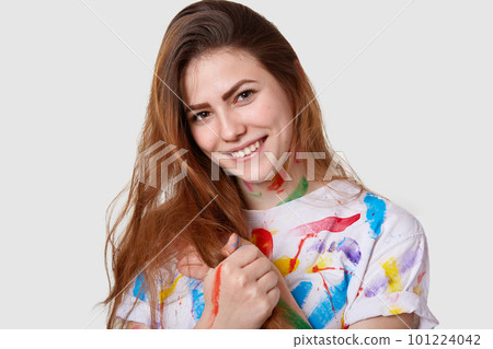 Photo of attractive young lady with dark hair, smiles gently, feels satisfied after drawing picture, glad to spend free time painting, isolated over white background. People, talent and creativity Photo of attractive young lady with dark hair, smiles gently, feels satisfied after drawing picture, glad to spend free time painting, isolated over white background. People, talent and creativity 101224042