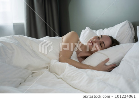 Beautiful attractive woman sleeps and has sweet dreams, lying on a bed in a cozy bedroom in the morning, feeling so relaxed and comfortable. 101224061