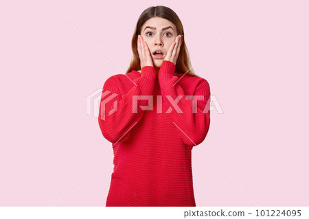 Waist up shot of surprised young woman touches cheeks, dressed in red jumper, expresses shock, poses over rosy background. Confused European girl looks in amazement. People and astonishment. Waist up shot of surprised young woman touches cheeks, dressed in red jumper, expresses shock, poses over rosy background. Confused European girl looks in amazement. People and astonishment. 101224095