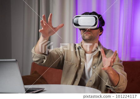 Young man wearing virtual reality glasses in a modern living room. Using a smartphone with a VR goggles headset. Young man wearing virtual reality glasses in a modern living room. Using a smartphone with a VR goggles headset. 101224117