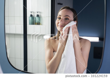 Facial skin care. An attractive woman wipes her clean face with a towel after washing in a modern bathroom. The concept of a morning body care procedure. Facial skin care. An attractive woman wipes her clean face with a towel after washing in a modern bathroom. The concept of a morning body care procedure. 101224159