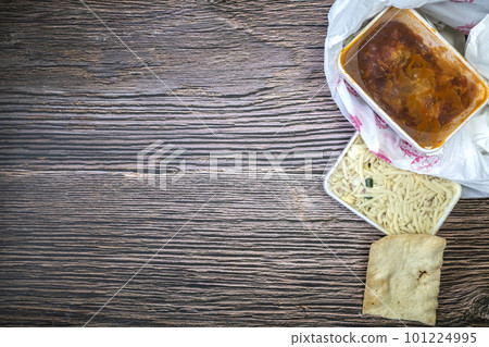 Chinese takeaway food selection in plastic bag. Bami, babi pangang, crispy shredded beef, sweet and sour chicken, krupuk top view on wooden table copy space. Food delivery 101224995