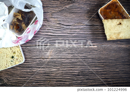Chinese takeaway food selection in plastic bag. Bami, babi pangang, crispy shredded beef, sweet and sour chicken, krupuk top view on wooden table copy space. Food delivery 101224996