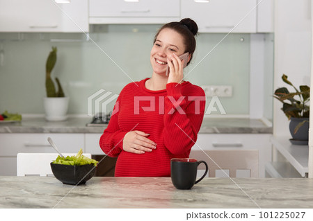 Photo of happy laughing brunette woman sitting in kitchen and speaking via smart phone with friend or huband, female waits for baby. Pregnant woman spending time at at home. Technology concept. Photo of happy laughing brunette woman sitting in kitchen and speaking via smart phone with friend or huband, female waits for baby. Pregnant woman spending time at at home. Technology concept. 101225027