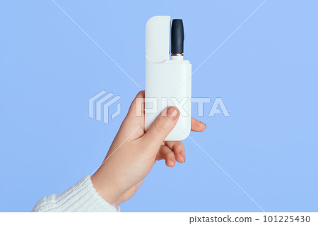 New technology of electronic cigarettes system of heating of tobacco, faceless female holding e ciggy in hand isolated over blue background, unknown person with device for smoking. New technology of electronic cigarettes system of heating of tobacco, faceless female holding e ciggy in hand isolated over blue background, unknown person with device for smoking. 101225430