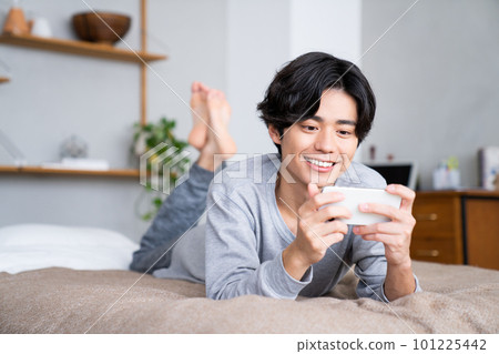 Young man watching smartphone in bed 101225442