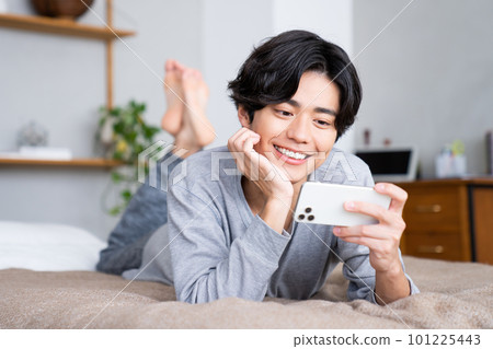Young man watching smartphone in bed Young man watching smartphone in bed 101225443