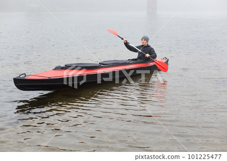 Concentrated man with oar in hands rowing boat in river in cold autumn day, water sport, guy wearing grey cap and and black jacket spending his spare time in active way. 101225477