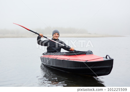 Autumn kayaking on river, smiling handsome man with paddle in hands looking directly at camera, enjoying spending time in open air while rowing boat. Autumn kayaking on river, smiling handsome man with paddle in hands looking directly at camera, enjoying spending time in open air while rowing boat. 101225509