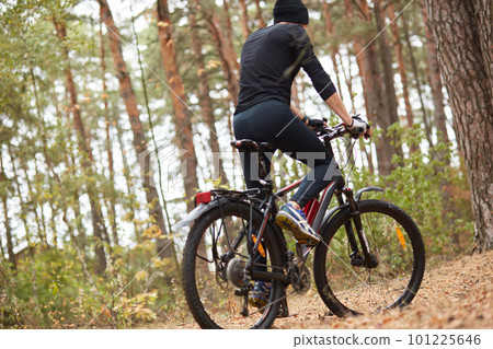 Image of young guy on mountain bike in forest, man posing backwards, handsome male wearing black sportwear and cap, spendig time in wood, enjoying fresh air. Healthy lifestyle and sport concept. Image of young guy on mountain bike in forest, man posing backwards, handsome male wearing black sportwear and cap, spendig time in wood, enjoying fresh air. Healthy lifestyle and sport concept. 101225646