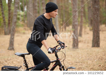 Image of young handsome rider wearing black sport wear and cap, riding his modern bike in forest, spending his spare time in active way, enjoing fresh air, male rides bike. Healthy lifestyle concept. Image of young handsome rider wearing black sport wear and cap, riding his modern bike in forest, spending his spare time in active way, enjoing fresh air, male rides bike. Healthy lifestyle concept. 101225652