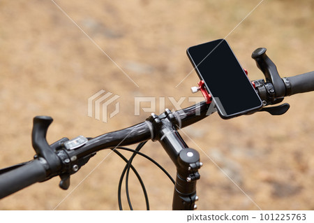 Black handlebar of sport bicycle over forest road background, having smartphone attached to right side, movement along road, gps navigator, going according to online map. Orientation concept. 101225763