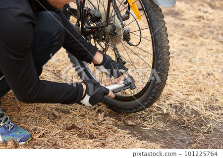 Close up of man hands pumping bicycle wheel, home maintenance of bike, bicycle service and maintaining for new season, faceless picture of wheel with flat tire, male reparing his bike in open air. 101225764