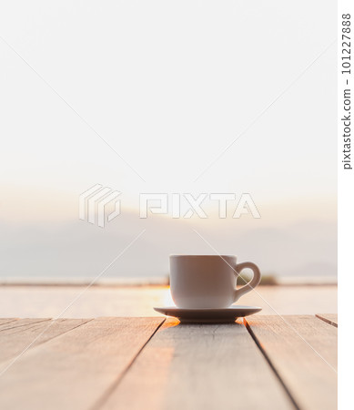 Cup of coffee on wooden deck over sunrise with river mountain in background. 101227888