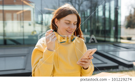 Young woman listening to music via headphones on the street. Pretty happy redhead woman standing on urban background and holding a mobile phone. 101229274
